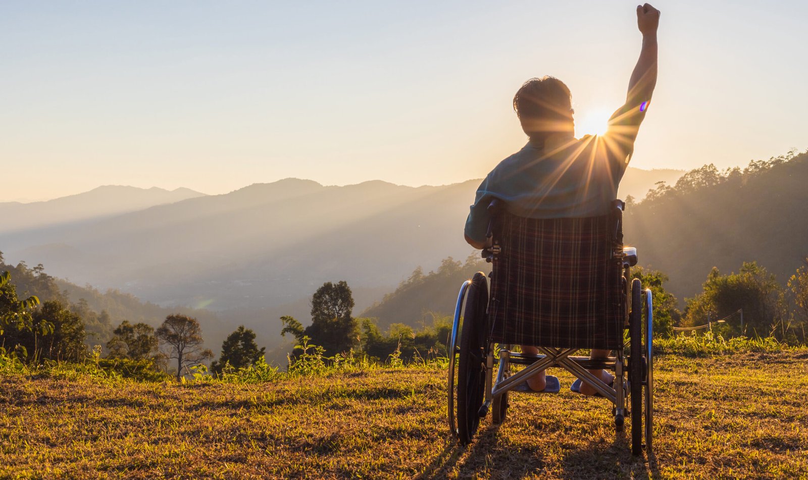 Silhouette of happy disabled man in a wheelchair and stretching hands at sunset. back view,